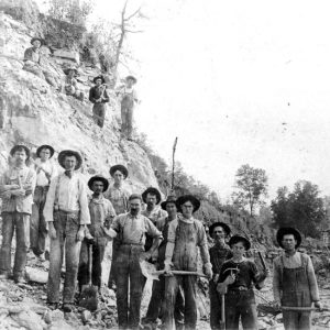 White men wearing hats posing on a hillside with mining tools