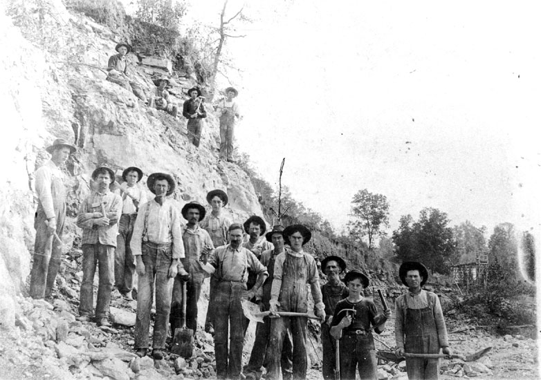 White men wearing hats posing on a hillside with mining tools