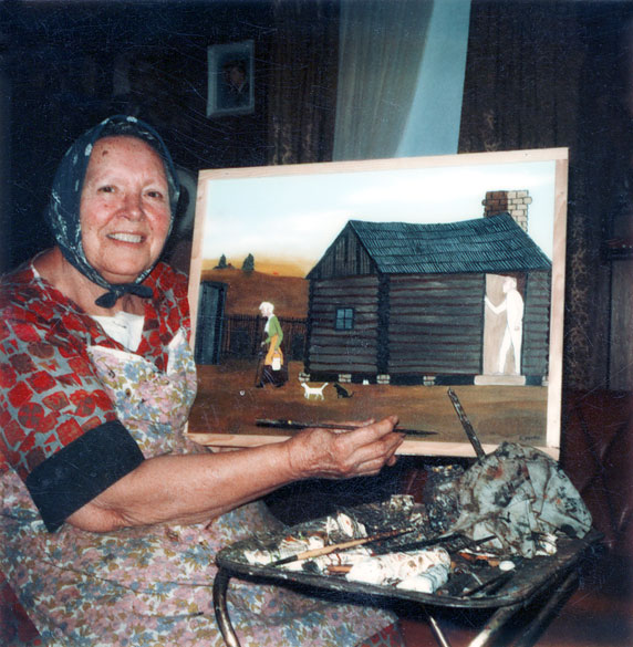 White woman holding a painting of a log cabin with woman and man