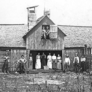 White men and women posing in front of a long wooden building