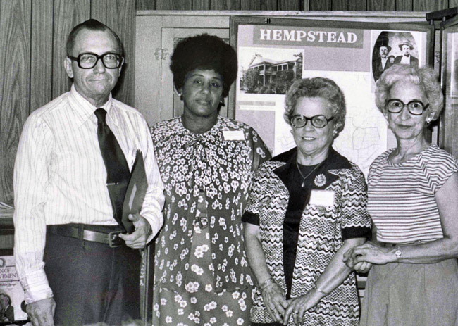 White man in glasses standing with African-American woman in a dress and two white women wearing glasses