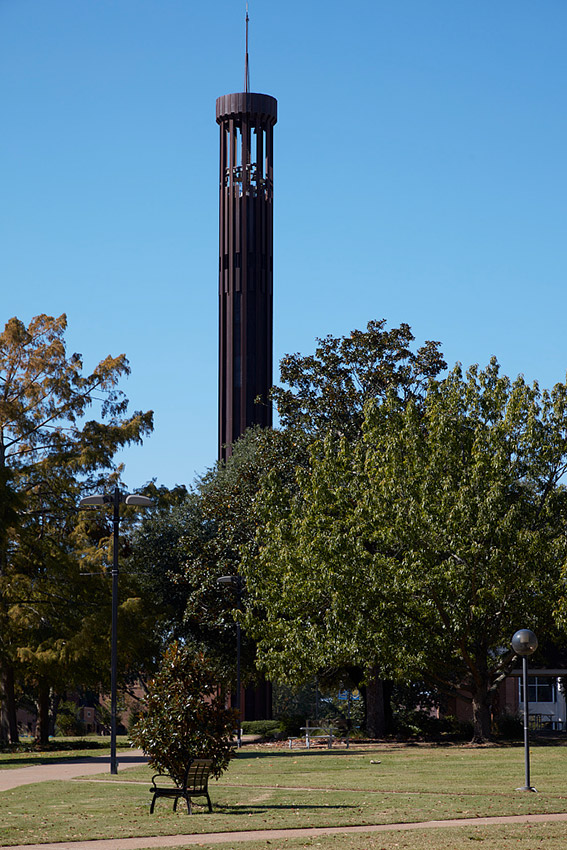 Round bell tower on college campus with trees and walking paths with benches and buildings under it