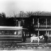 People pose outside two story building with "Huddlestons Hotel" sign on balcony and tracks with horse and streetcar