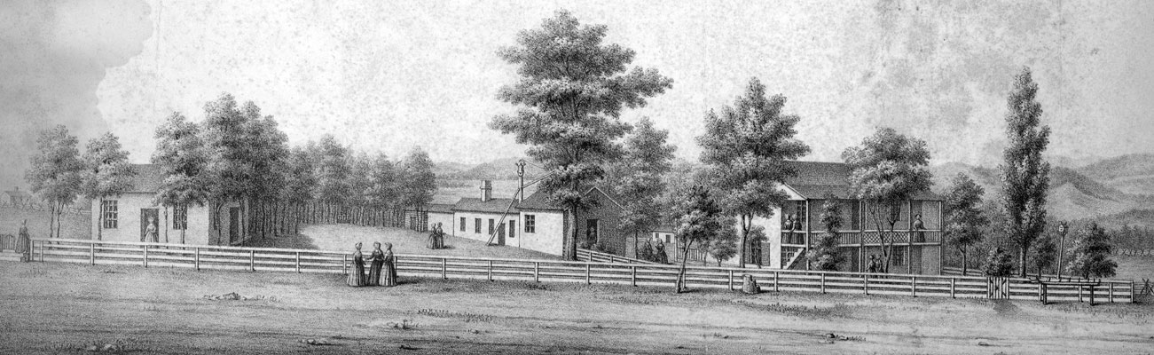 Women in dresses talking by a fence with schoolhouse and trees