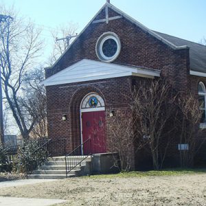 Brick church building with red front doors round stained glass window and white statue