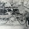 Group of white men and women sitting on horse drawn wagon