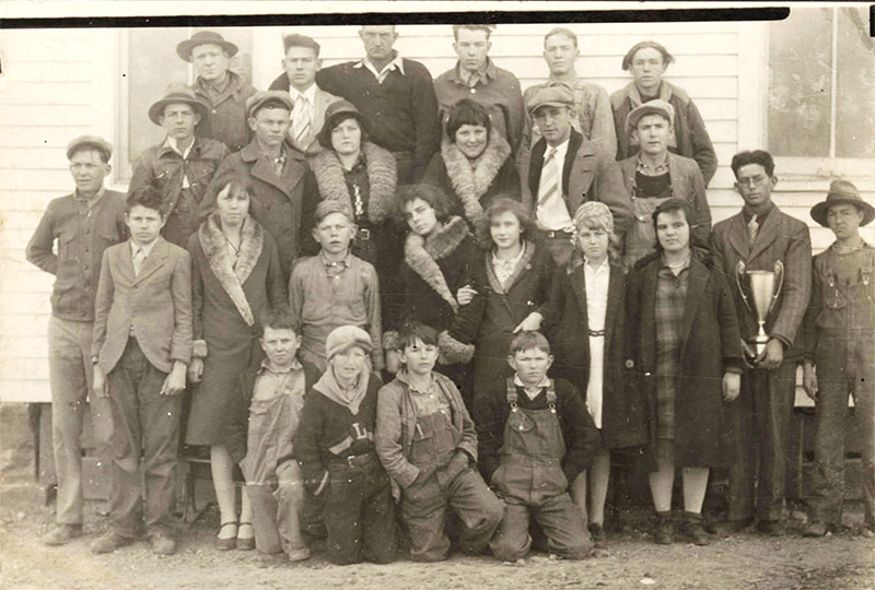 Group of young white men women and children posing with trophy outside building with wood siding