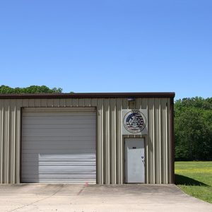 Building with two garage bays with sign above the door and propane tank beside it on grass