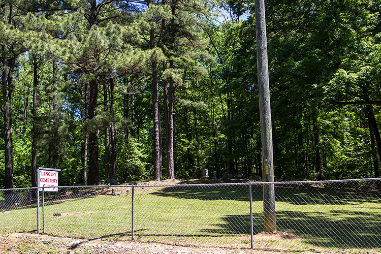 Fenced-in cemetery with hanging sign trees and telephone pole in it