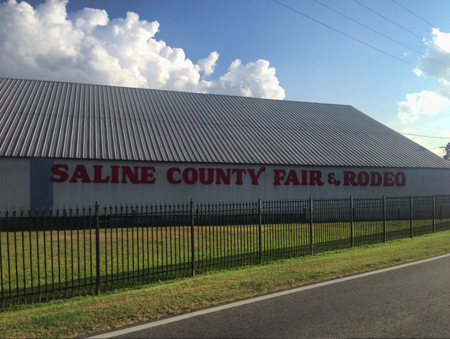 Metal building with "Saline County Fair and Rodeo" painted on the side and iron fence on street