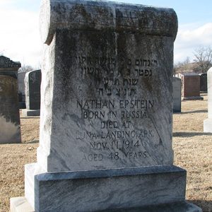 Headstone with inscription in English and Hebrew in cemetery with bare trees and brown grass