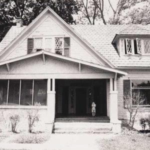 Two-story house with covered porch with child standing on porch
