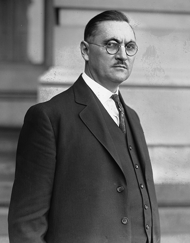 White man with glasses and mustache in suit and tie