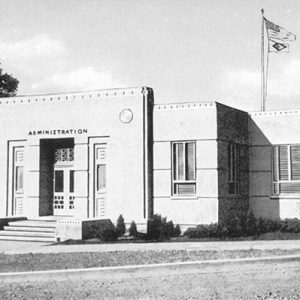 Single-story "administration" building with flags flying in the background above it