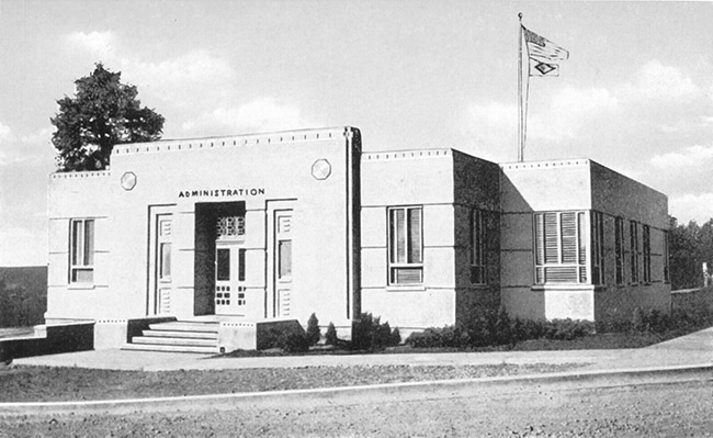 Single-story "administration" building with flags flying in the background above it