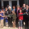 White men women and children cutting ribbon with large scissors