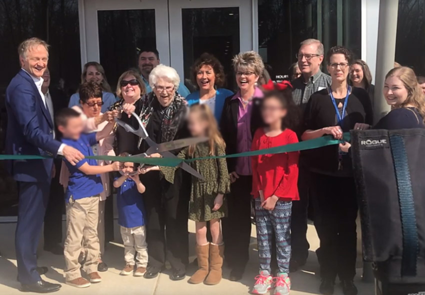 White men women and children cutting ribbon with large scissors