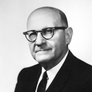 Bald white man with black-framed glasses in suit and tie