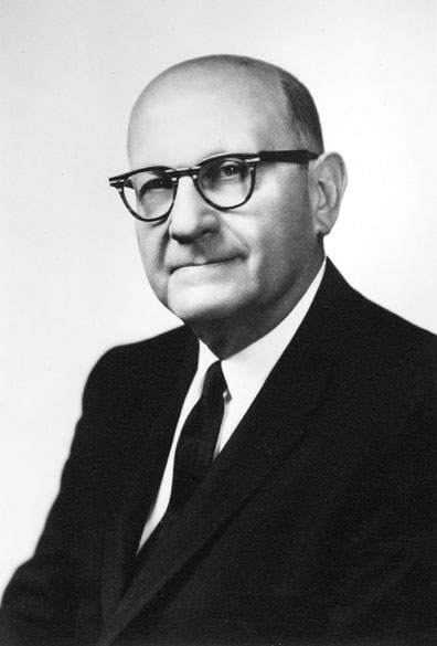 Bald white man with black-framed glasses in suit and tie