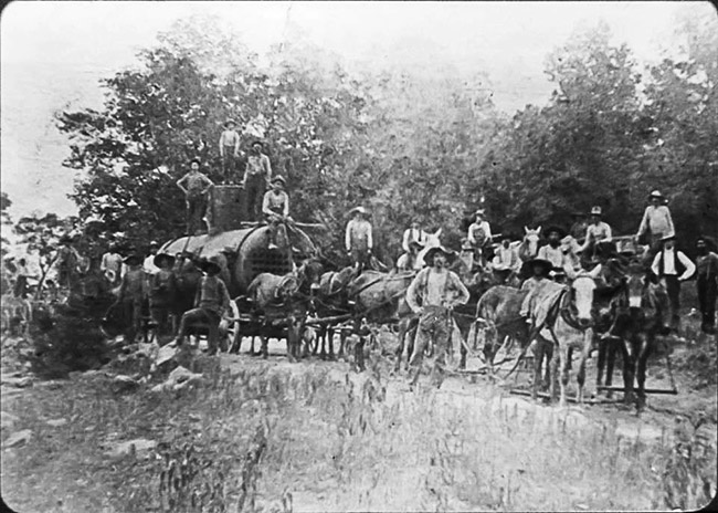 Group of white men with horses pulling boiler tank on wagon