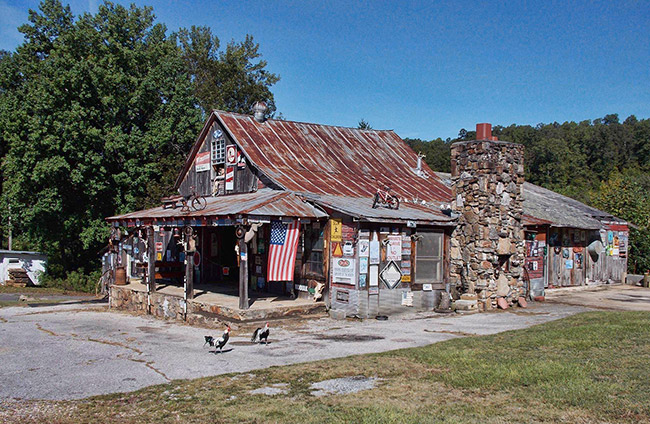 Storefront building with rusted metal roof stone chimney and covered porch on parking lot