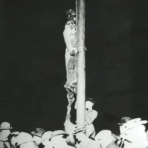 body of African American man hanging from pole with white men in hats standing under him