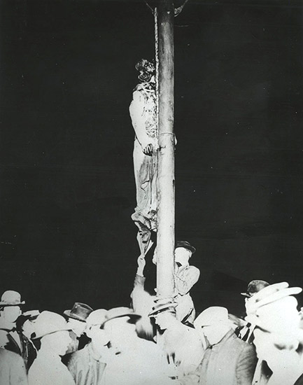 body of African American man hanging from pole with white men in hats standing under him