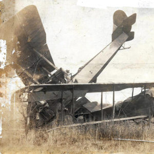 Biplane nose down atop other damaged biplane in field