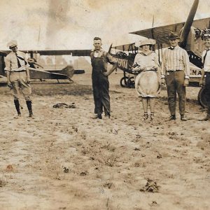 White men and woman in field with biplanes