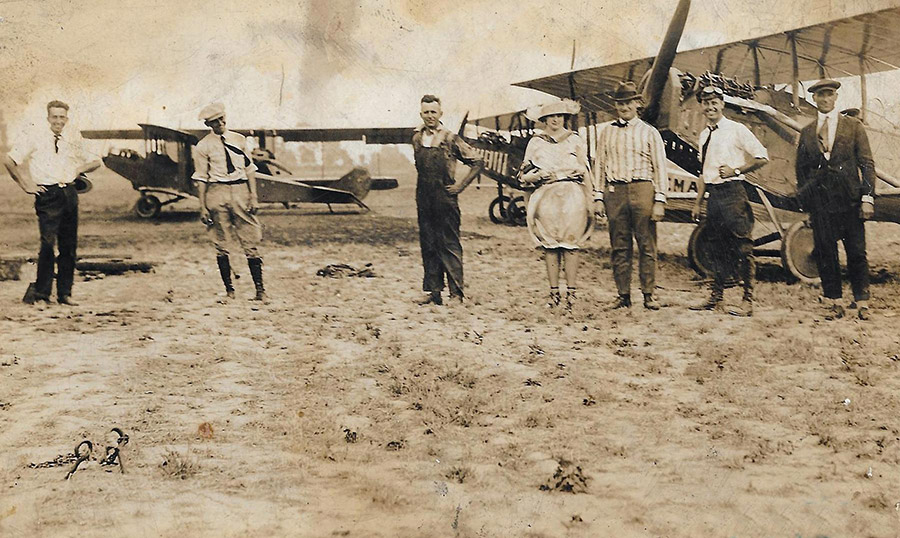 White men and woman in field with biplanes