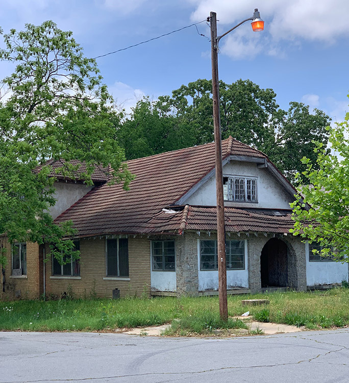 Abandoned brick house with arched doorway on street corner
