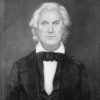 White man with long white hair in suit and bow tie