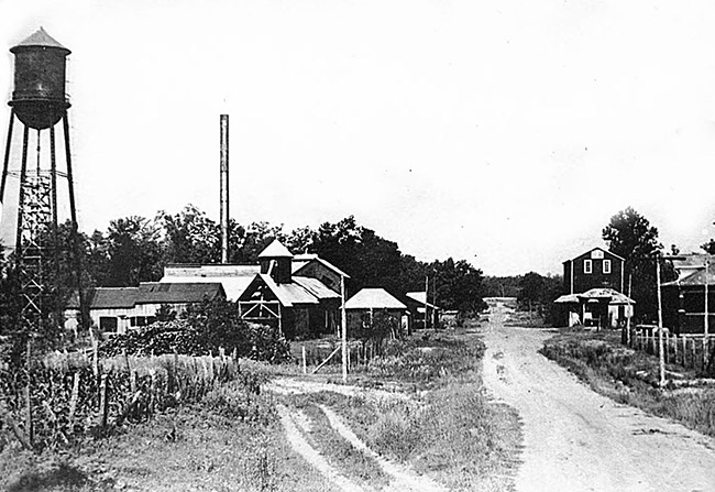 Industrial buildings on dirt road with water tower and smoke stacks