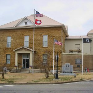 Multistory stone building with flag pole and stone memorial in front yard on street
