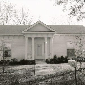 Front view of single-story house with four front columns sidewalk and mailbox in the foreground