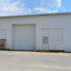 Loading bay area of single-story store building with windows and garage door on parking lot