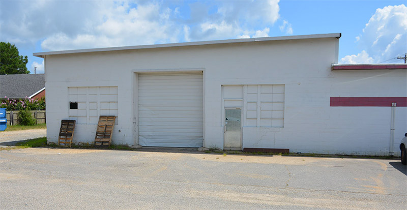 Loading bay area of single-story store building with windows and garage door on parking lot