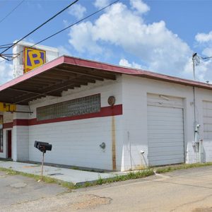 Front and side view of single-story store building with awnings on street under power lines
