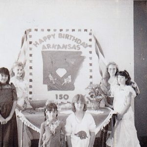 White children posing before large birthday cake "Happy Birthday Arkansas 150"