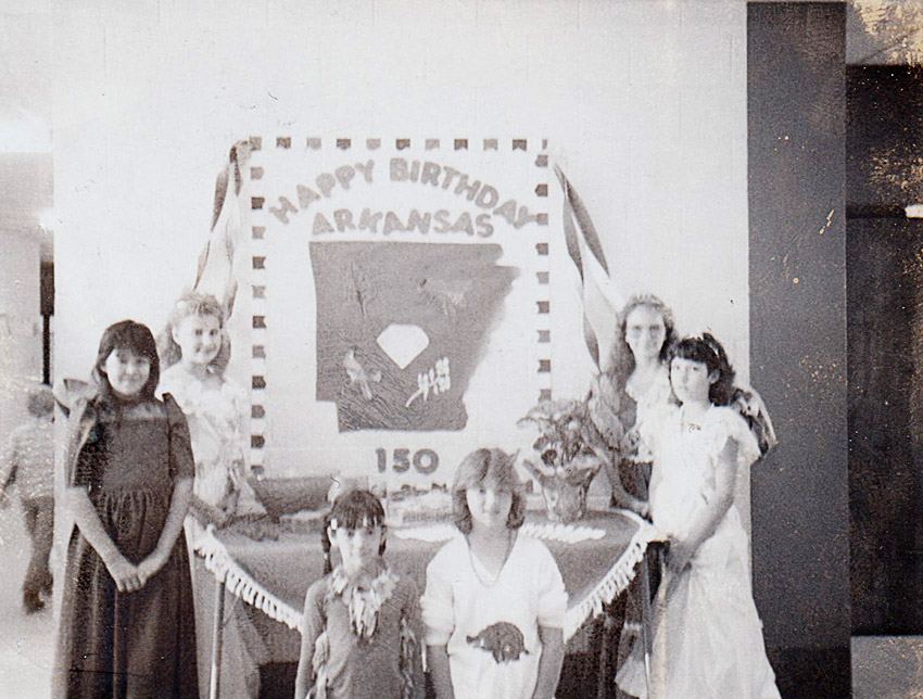 White children posing before large birthday cake "Happy Birthday Arkansas 150"