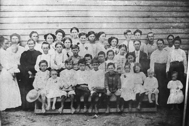 Group of white children and teachers standing outside building with wood siding