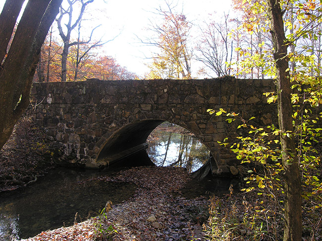 Side view of stone arch bridge over river under autumn trees