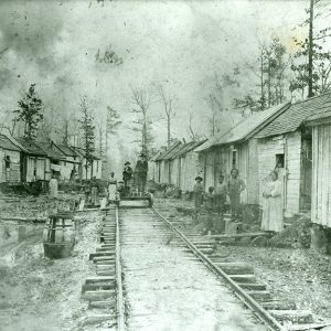 Railroad tracks running between two rows of shacks and African Americans standing outside