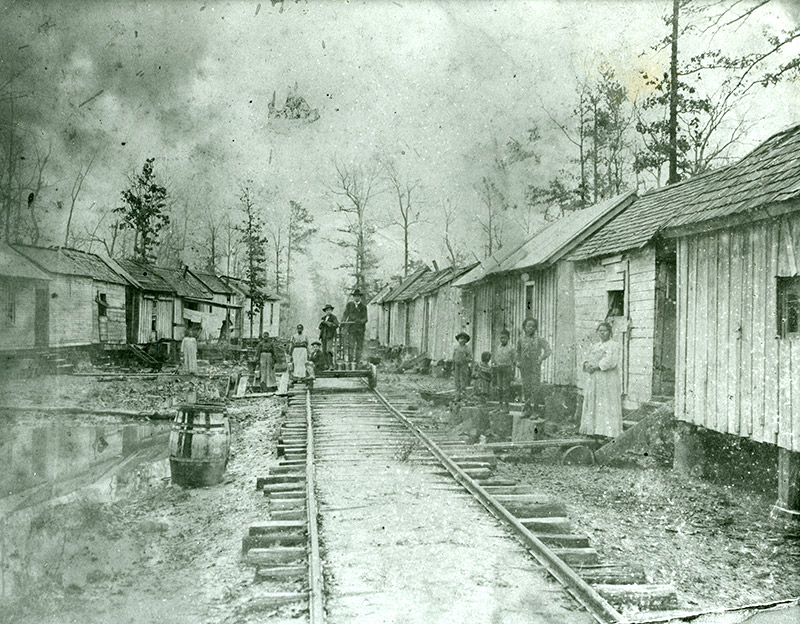 Railroad tracks running between two rows of shacks and African Americans standing outside