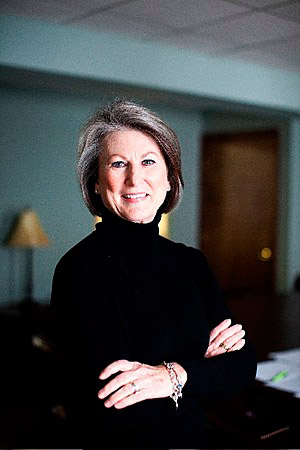 White woman smiling in black turtleneck sweater with arms crossed