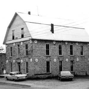 Barn-shaped stone three-story building on street with parked cars