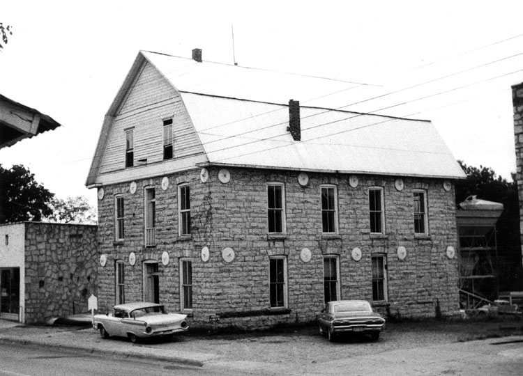 Barn-shaped stone three-story building on street with parked cars