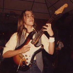 Young white man with long hair playing Fender Stratocaster electric guitar