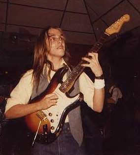 Young white man with long hair playing Fender Stratocaster electric guitar