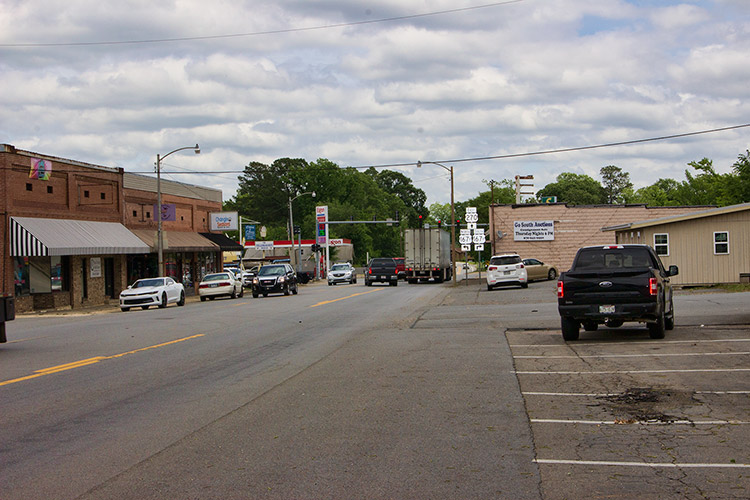 Town street with traffic brick storefronts and service station on the left and buildings on the right